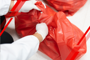 Two people in white gloves seal a red garbage bag during cleanup operation.