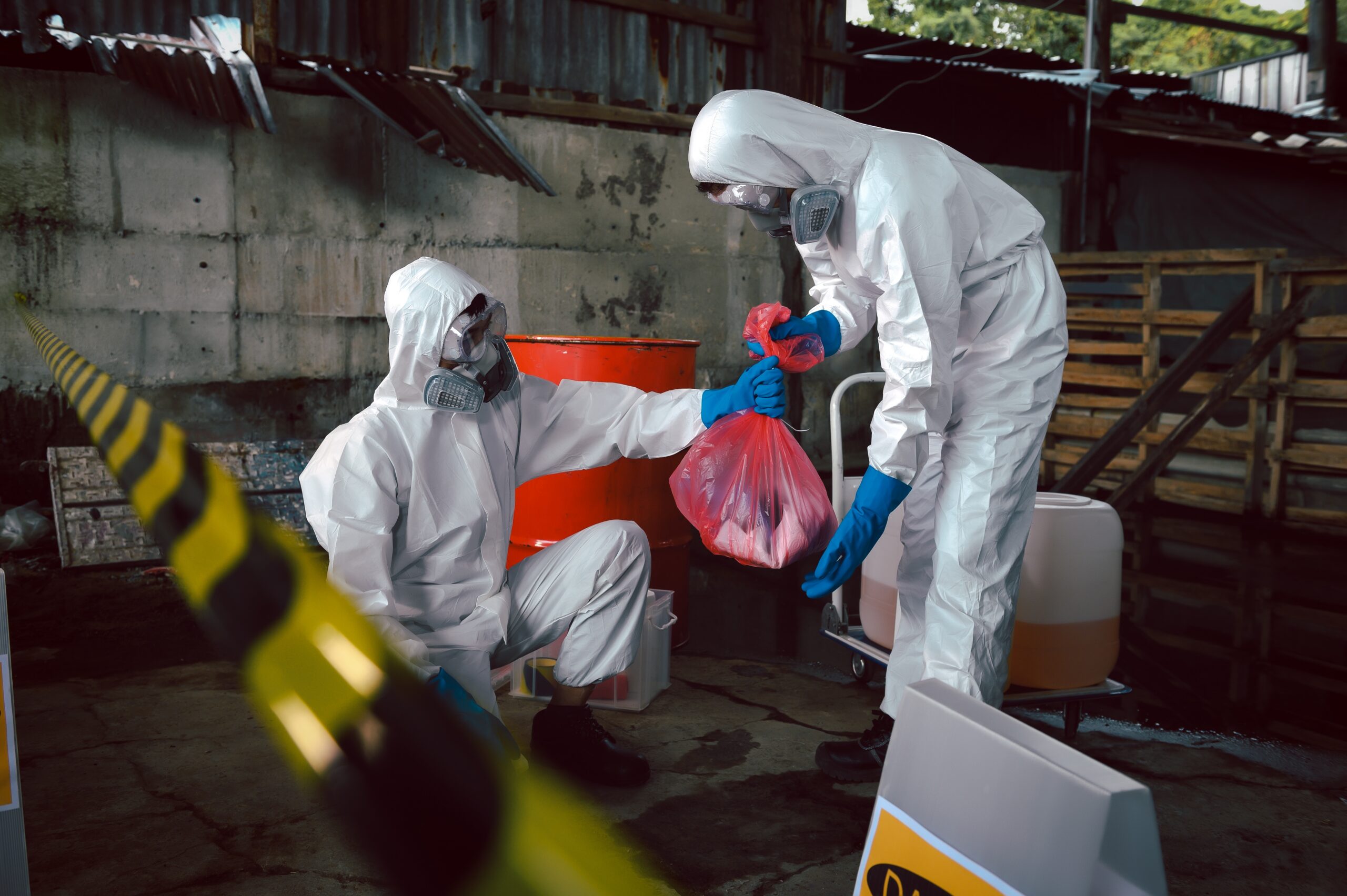 Person in a white hazmat suit and mask disinfecting a hospital hallway with a cleaning cart nearby.