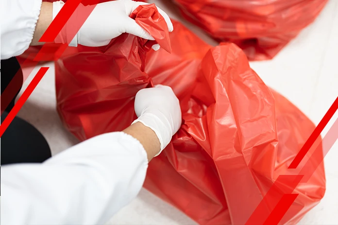 Two people in white gloves seal a red garbage bag during cleanup operation.