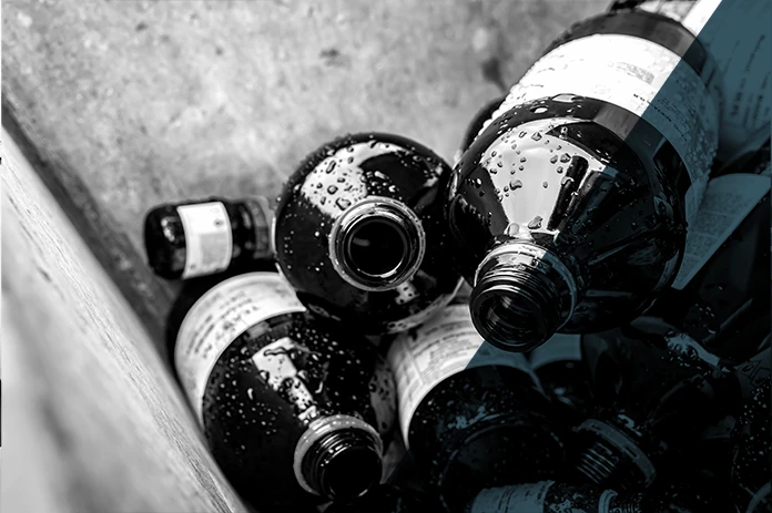 Several empty glass bottles with labels lie in a box, wet and dark in grayscale.